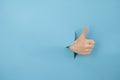 A woman's hand sticking out of a hole from a blue background shows a thumbs up. Royalty Free Stock Photo