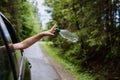 Woman& x27;s hand throwing away plastic bottle from car window on the road in green nature, environmental protection Royalty Free Stock Photo