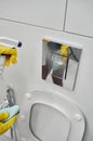 A woman's hand in yellow rubber gloves sprays a cleaning agent on the toilet flush button. Sanitization in the