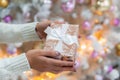 Woman& x27;s hands with gift box near Christmas tree, closeup. Present in hands in new year decoration