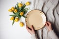 Woman& x27;s hands holding beige ceramic empty plate, yellow tulips on the background, flatlay, mockup. Generative AI
