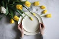 Woman's hands holding white empty plate, yellow tulips on the background, flatlay, mockup. Generative AI