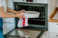 Woman& x27;s hands putting white bakery dish into an oven