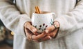 Woman& x27;s hands in sweater holding cup mug with cinnamon of hot drink coffee indoors. Still life composition. Royalty Free Stock Photo