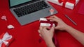 Woman's hands unpack the gift box, undoing bow. Top view of red table with laptop, gifts, hearts and valentine. Romantic