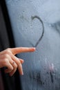 A woman& x27;s hand draws the shape of a heart on the fogged window.