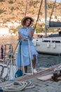 Woman yacht sea. A young happy woman in a blue dress and hat stands near the seaport with luxury yachts. Travel and