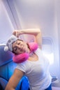 Woman yawns while sitting on the plane with a mask and a pillow for sleeping.