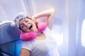 Woman yawns while sitting on the plane with a mask and a pillow for sleeping.