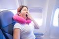 Woman yawns while sitting on the plane by the window.