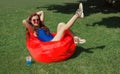 Young woman is relaxing in the hot summer on a ottoman on the grass, listening to music and taking photos