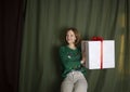 woman 35-40 years old holding a large white gift box tied with a red bow on a dark green background Royalty Free Stock Photo