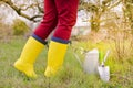 Woman in yellow boots in the garden. Focus on flowering tree branches. Shoes, watering can and spatula. The flowering