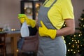 Woman in a yellow glove holds a bottle of detergent and shows like sigh on the background of New Year`s lights.