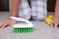 Woman in yellow gloves with a green brush cleaning and brushing carpet, removing stains and wool from it and doing routine Royalty Free Stock Photo