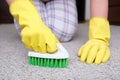 Woman in yellow gloves with a green brush cleaning and brushing carpet, removing stains and wool from it and doing Royalty Free Stock Photo