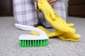 Woman in yellow gloves with a green brush cleaning and brushing carpet, removing stains and wool from it and doing routine Royalty Free Stock Photo