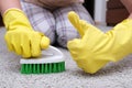 Woman in yellow gloves with a green brush showing thumb up while cleaning and brushing carpet, removing stains and wool Royalty Free Stock Photo