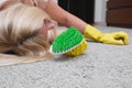 Woman in yellow gloves with a green brush is so tired of cleaning and brushing carpet, removing stains and wool from it Royalty Free Stock Photo