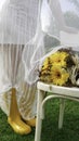 Woman in yellow gumboots and white spring dress next to a wooden chair and bouquet of yellow Gerbera daisy