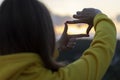 A woman in a yellow hoodie looks at the sunset through a finger frames.