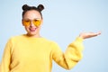 A woman in a yellow jacket on a blue background with an open palm gestures. copy space