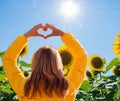 Woman in a yellow jacket making a heart shape with her hands on a sunflower field Royalty Free Stock Photo