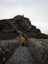 Woman in yellow jacket on stone staircase footbridge to Gaztelugatxe islet rock castle hermitage Bermeo Basque Spain