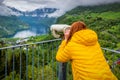 Woman in yellow looking throw the telescope on Geiranger fjord