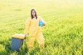 A woman in a yellow protective suit stands in the middle of a green field holding a globe, and with her other hand carries a Royalty Free Stock Photo