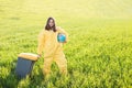 A woman in a yellow protective suit stands in the middle of a green field holding a globe, and with her other hand carries a Royalty Free Stock Photo