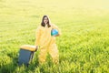 A woman in a yellow protective suit stands in the middle of a green field holding a globe, and with her other hand carries a Royalty Free Stock Photo