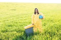 A woman in a yellow protective suit stands in the middle of a green field holding a globe, and with her other hand carries a Royalty Free Stock Photo