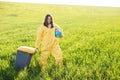 A woman in a yellow protective suit stands in the middle of a green field holding a globe, and with her other hand carries a Royalty Free Stock Photo