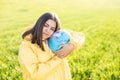 A woman in a yellow protective suit stands in the middle of a green field holding a globe. The concept of saving the planet from