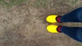 Woman in yellow rubber galoshes stands on the ground in a garden