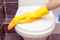 Woman in yellow rubber gloves cleaning toilet seat cover with orange cloth. Bathroom and toilet hygiene. Royalty Free Stock Photo