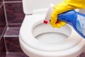 Woman in yellow rubber gloves cleaning toilet seat cover with orange cloth and detergent. Royalty Free Stock Photo