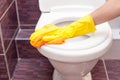 Woman in yellow rubber gloves cleaning toilet seat with orange cloth. Bathroom and toilet hygiene. Royalty Free Stock Photo