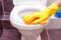 Woman in yellow rubber gloves cleaning toilet seat with orange cloth. Bathroom and toilet hygiene.