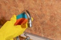 Woman in yellow rubber gloves washes a metal faucet with a sponge at the sink in the kitchen Royalty Free Stock Photo