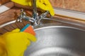 Woman in yellow rubber gloves washes a metal faucet with a sponge at the sink in the kitchen Royalty Free Stock Photo