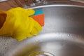 Woman in yellow rubber gloves washes a metal sink in the kitchen with a sponge Royalty Free Stock Photo