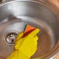 Woman in yellow rubber gloves washes a metal sink in the kitchen with a sponge Royalty Free Stock Photo