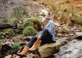 Woman in yellow shirt and hat sitting on stone in strem in the autumn forest