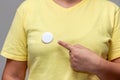 Woman in yellow shirt pointing at a shiny round button. Isolated pin badge mockup