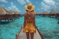 A woman in a yellow sun hat and dress gazes at the azure ocean from a dock Royalty Free Stock Photo