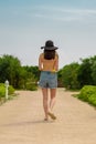 A woman in a yellow swimsuit and denim shorts and hat is on the path from the back Royalty Free Stock Photo