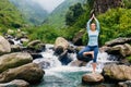 Woman in yoga asana Vrikshasana tree pose at waterfall outdoors