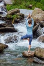 Woman in yoga asana Vrikshasana tree pose at waterfall outdoors